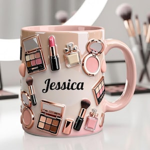 Könnte beinhalten: Eine rosa-beige Keramiktasse, verziert mit Make-up-Elementen, darunter Lidschattenpaletten, Lippenstifte und Parfümflaschen. Der Name "Jessica" steht in schwarzer Schrift auf der Vorderseite. Die Tasse hat einen passenden rosa Griff.
