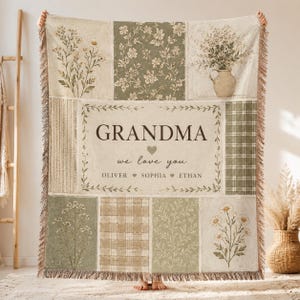 May include: A beige and green patchwork throw blanket with floral and plaid patterns. The center panel reads "GRANDMA we love you" with names below. The blanket has a fringed edge and is held up by a person.