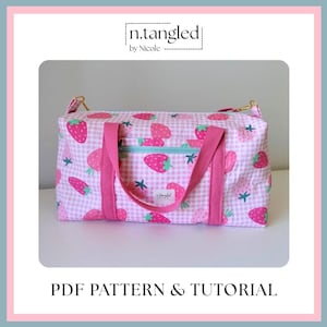 May include: A rectangular duffel bag featuring a pink and white gingham pattern with a strawberry print. The bag has pink fabric handles, a light blue zippered front pocket, and gold-tone hardware. A label reads n.tangled by Nicole.