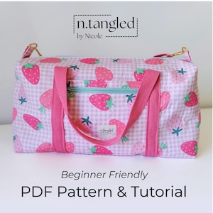 Pode incluir: Uma mala de viagem com padrão xadrez vichy rosa e branco com estampa de morangos, alças de tecido rosa, zíper azul claro e ferragens douradas. A mala exibe o texto n.tangled by Nicole, Beginner Friendly e PDF Pattern & Tutorial.