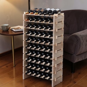 May include: A tall, light-colored wooden wine rack filled with numerous wine bottles. The rack has multiple shelves, each holding several bottles. The bottles are dark, with visible labels. The rack is positioned indoors, near a dark-colored armchair.