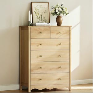 May include: A light-colored wooden dresser with six drawers and brass knobs. The top of the dresser has a framed picture, candles, and a vase of flowers. The dresser is a piece of bedroom furniture.