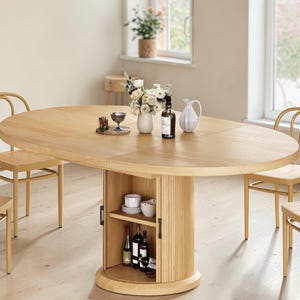 May include: Oval wooden dining table with a built-in storage cabinet. The table is light brown and surrounded by four wooden chairs. The cabinet has a shelf with wine bottles, glasses, and dishes. A vase of flowers and other decorative items are on the table.