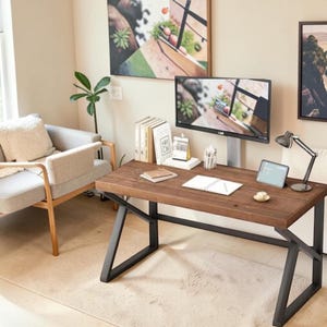 May include: A rectangular wooden desk with a dark brown finish and a black metal frame featuring angled legs. The desk surface holds a computer monitor, a small tablet, a desk lamp, a notebook, a pen holder, and several books with white spines.
