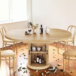 May include: A light wood round dining table with a built-in wine cabinet. The table is surrounded by four light wood chairs. The table is set with wine bottles, glasses, and a vase of flowers. The floor is scattered with white flower petals.