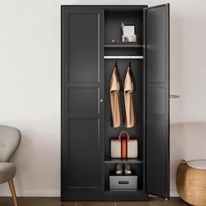May include: A tall, matte black wardrobe with two doors, one of which is open. The interior features a top shelf with small items, a hanging rod with two tan shirts, a middle shelf with a beige handbag, and a bottom shelf with a gray storage box.