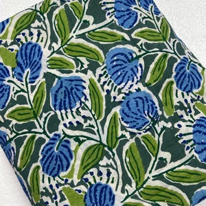 Op de afbeelding: Een gevouwen stuk stof met een donkergroene achtergrond en een herhalend patroon van blauwe bloemen en lichtgroene bladeren. Het bloemmotief bevat witte accenten en stengels, wat zorgt voor een dichte botanische print op het textieloppervlak.