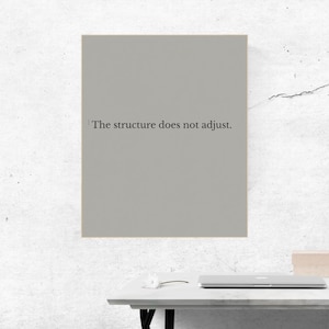 Op de afbeelding: Een ingelijste print met de tekst "The structure does not adjust" in zwarte letters op een grijze achtergrond. De print wordt weergegeven op een wit bureau met een laptop en een kleine doos.