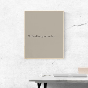 Peut inclure: Un cadre avec un fond taupe et un fin cadre marron clair. Le texte "No deadline governs this" est centré en noir. L'impression est affichée sur un bureau blanc avec un ordinateur portable et une petite boîte.