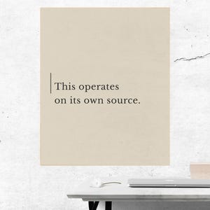 Op de afbeelding: Een beige poster met de tekst "This operates on its own source." De poster is aan een witte muur bevestigd. Op de voorgrond staat een witte bureau met een laptop en een klein decoratief item.