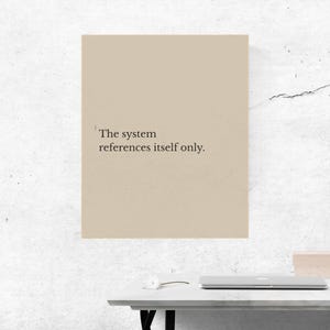 May include: A beige rectangular print with the text "The system references itself only." The print is displayed on a white table with a laptop and a small box.
