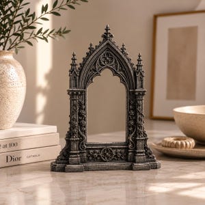 May include: A dark grey, weathered stone-effect picture frame featuring intricate Gothic architectural details, including pointed arches, slender columns, and relief carvings of climbing roses and circular floral motifs on the base and sides.