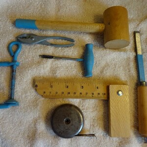 May include: A set of woodworking tools including a wooden mallet, a ruler, a metal tape measure, a clamp, a chisel, a drill bit, and a pair of pliers.