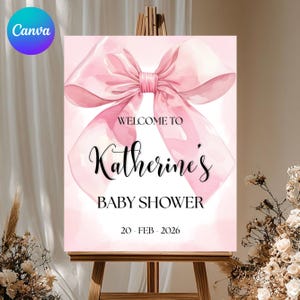 May include: A pink baby shower sign with a large watercolor bow. The sign reads "Welcome to Katherine's Baby Shower" and the date "20 - FEB - 2026". The sign is displayed on a wooden easel.