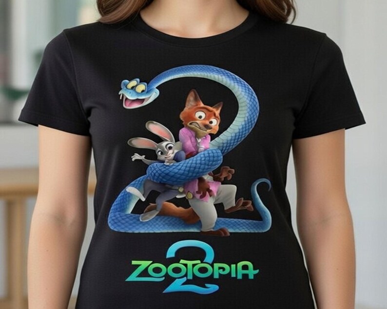 Peut inclure: T-shirt noir avec un graphisme color&eacute; des personnages du film d'animation Zootopia. Le motif comprend un serpent bleu enroul&eacute; autour d'un renard et d'un lapin, avec l'inscription "Zootopia 2" en turquoise et vert.