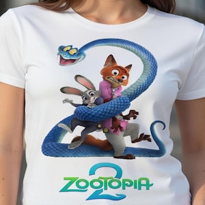 Peut inclure: T-shirt blanc avec un motif color&eacute; du film d'animation Zootopie. Le design pr&eacute;sente les personnages Judy Hopps, Nick Wilde et un serpent bleu formant le chiffre 2, avec le titre du film en dessous.