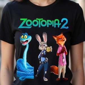 Peut inclure: T-shirt noir avec des personnages de Zootopie 2. Le motif comprend un serpent bleu, un lapin en uniforme de policier et un renard en chemise rose. Les mots "ZOOTOPIA 2" sont imprim&eacute;s en vert et bleu en haut.