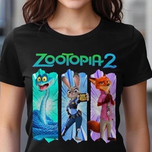 Peut inclure: T-shirt noir avec le texte "Zootopia 2" en vert et bleu sarcelle. Le motif pr&eacute;sente trois personnages de dessins anim&eacute;s : un serpent bleu, un lapin en uniforme de policier et un renard en chemise rose. Les personnages sont sur un fond color&eacute;.