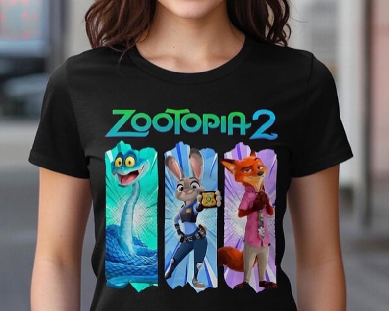 Peut inclure: T-shirt noir avec le texte "Zootopia 2" en vert et bleu sarcelle. Le motif pr&eacute;sente trois personnages de dessins anim&eacute;s : un serpent bleu, un lapin en uniforme de policier et un renard en chemise rose. Les personnages sont sur un fond color&eacute;.