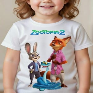 Peut inclure: T-shirt blanc avec des personnages de Zootopia 2. Le design comprend Judy Hopps, Nick Wilde et un serpent bleu. Le texte "Zootopia 2" est imprim&eacute; en vert et bleu au-dessus des personnages.