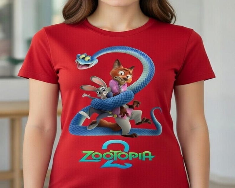 Peut inclure: T-shirt rouge avec un graphisme color&eacute; du film d'animation "Zootopia 2". Le motif comprend un serpent bleu, un renard et un lapin, avec le titre du film en vert et bleu. Le t-shirt est &agrave; manches courtes.