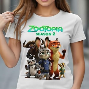 Peut inclure: T-shirt blanc avec une illustration color&eacute;e des personnages de Zootopie, dont Judy Hopps et Nick Wilde, et le texte "Zootopia Saison 2". Le design est une illustration des personnages du film d'animation.