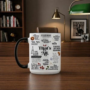 May include: A white ceramic mug with a black handle, featuring various phrases and illustrations in black. The mug includes text such as "That's All" and "Oh, It's for Paris."