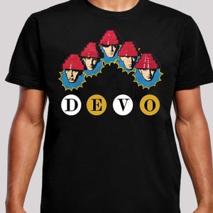 May include: Black t-shirt featuring a graphic of five figures wearing red hats and blue collars. The word "DEVO" is printed in a circle design below the figures. The design is in a retro style.