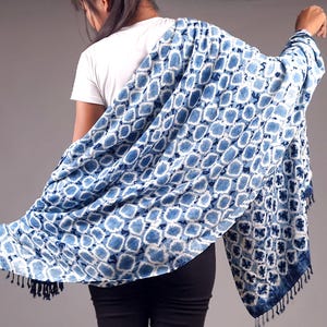 Peut inclure: Un châle rectangulaire présentant un motif tie-dye bleu et blanc avec des cercles répétitifs. Le tissu a un aspect souple et drapé, et est agrémenté de petites franges bleu foncé le long des bords inférieurs du textile.