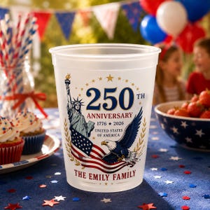 May include: A clear plastic cup featuring a design commemorating the 250th anniversary of the United States. The design includes the Statue of Liberty, an eagle, and the American flag. The text reads "250th Anniversary 1776-2026 United States of America" and "The Emily Family".