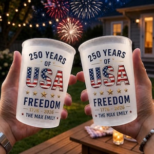 May include: Two frosted plastic cups with the text "250 Years of USA Freedom 1776-2026". The cups feature a red, white, and blue USA flag design. Fireworks are visible in the background.