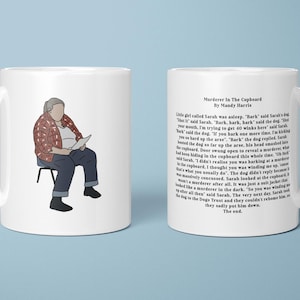 May include: White ceramic mug with an illustration of a person reading, wearing a red plaid shirt and blue trousers. The other side of the mug has text from a story titled "Murderer in the Cupboard" by Mandy Harris.