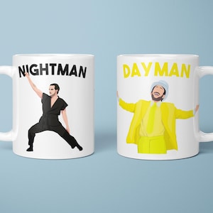 May include: Two white ceramic mugs with black and yellow text and illustrations. One mug says "NIGHTMAN" and features a figure in black. The other says "DAYMAN" and features a figure in yellow. Both mugs have white handles.