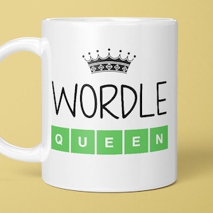 May include: White ceramic mug featuring the word "WORDLE" in black script, with a black crown graphic above. The word "QUEEN" is spelled out in green letter tiles below. The mug has a white handle and is set against a yellow background.