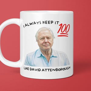 May include: White ceramic mug with a portrait of David Attenborough. The mug has the text "I ALWAYS KEEP IT 100 LIKE DAVID ATTENBOROUGH" in black and red. The mug is set against a red background.