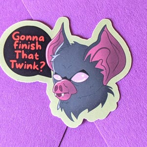May include: A sticker featuring a cartoon bat with pink eyes, ears, and snout. The bat is dark gray with a light green outline. A speech bubble says, "Gonna finish that twink?" in red and white text.