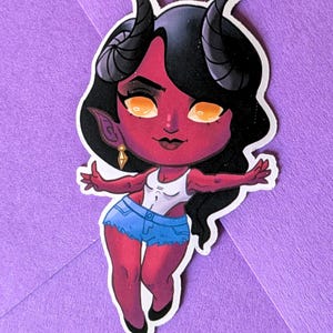 May include: A sticker featuring a cartoon illustration of a female demon with red skin, black hair, and horns. She wears a white top, denim shorts, and black shoes. The demon has yellow eyes and a gold earring. The sticker is on a purple background.