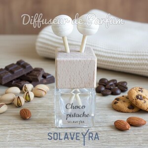 May include: A clear glass bottle with a wooden top and two white lollipop-shaped diffusers. The bottle is labeled "Choco pistache" and surrounded by chocolate, pistachios, coffee beans, cookies, and almonds. The text "SOLAVEYRA" is at the bottom.