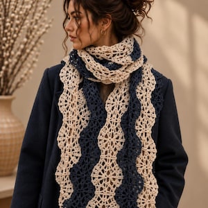 Puede incluir: Una bufanda de ganchillo larga y bicolor con un intrincado patrón calado repetitivo. La bufanda está construida con bandas verticales onduladas que alternan hilo color crema y azul marino oscuro, drapeada sobre el cuello sobre un abrigo azul marino.