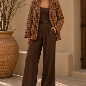 May include: A brown crochet blazer with a geometric open-knit pattern, notched lapels, and two front pockets. The blazer is worn over a dark brown sleeveless top and high-waisted wide-leg trousers, cinched with a thin matching brown belt.
