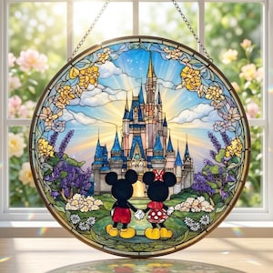 Op de afbeelding: Ronde glas-in-loodraam met een kasteelscène met Mickey en Minnie Mouse. Het kunstwerk heeft een blauwe lucht met een gouden kasteel, omgeven door bloemmotieven. Het raam hangt voor een raam.