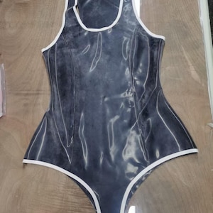 May include: A sleeveless bodysuit in a dark, semi-translucent charcoal gray with a glossy finish. The garment features a high-cut leg design and a scoop neckline, accented throughout with crisp white piping along all the edges and seams.