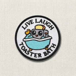 May include: Embroidered patch with a white background and a black border. The patch features a cartoon toaster in a blue bathtub with a rubber ducky. The text "LIVE LAUGH TOASTER BATH" is in a circular pattern around the image.