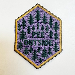 May include: A purple embroidered patch with a forest design and the words "I PEE OUTSIDE" in green. The patch has a gold border and a hexagonal shape, perfect for outdoor enthusiasts.
