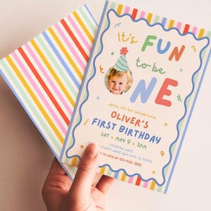 Op de afbeelding: Een verjaardagsuitnodiging met de tekst "It's FUN to be ONE" in kleurrijke letters. De uitnodiging bevat een foto van een baby met een feesthoedje en bevat evenementdetails. De achterkant van de uitnodiging heeft kleurrijke verticale strepen.