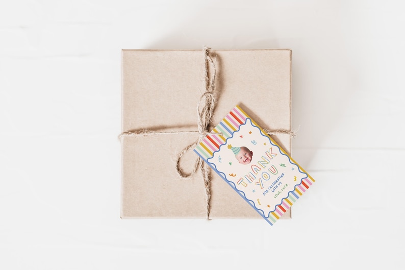 Pu&ograve; includere: Una scatola regalo quadrata in cartone marrone legata con spago di juta naturale, con un'etichetta rettangolare a righe verticali colorate, bordo blu smerlato e il testo THANK YOU FOR CELEBRATING WITH US LOVE, LUCY con foto di un neonato.