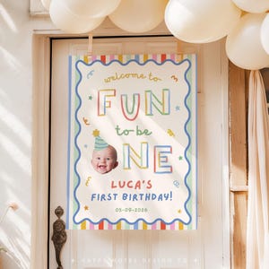 Pu&ograve; includere: Un cartello di compleanno rettangolare con un bordo blu smerlato e bordi a righe colorate. Il testo recita "welcome to FUN to be ONE" con la foto di un bambino con un cappellino da festa. Sotto, "LUCA'S FIRST BIRTHDAY" e "05-09-2026".