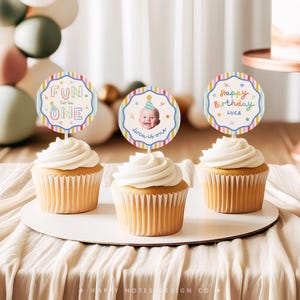 Pu&ograve; includere: Tre cupcake sormontati da decorazioni rotonde in carta con bordi a righe colorate. La decorazione a sinistra riporta Fun to be ONE, quella centrale mostra la foto di un bambino con cappellino da festa e il testo Luca is one, quella a destra Happy Birthday LUCA.