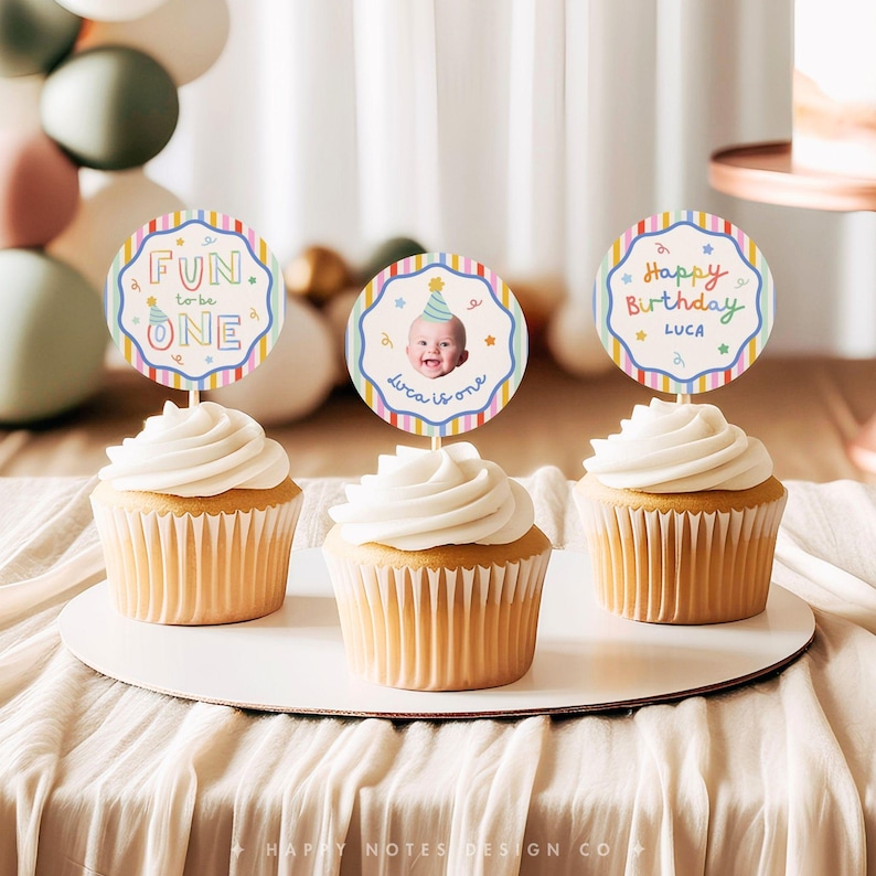 Pu&ograve; includere: Tre cupcake sormontati da decorazioni rotonde in carta con bordi a righe colorate. La decorazione a sinistra riporta Fun to be ONE, quella centrale mostra la foto di un bambino con cappellino da festa e il testo Luca is one, quella a destra Happy Birthday LUCA.