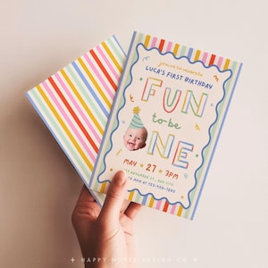 Pu&ograve; includere: Un biglietto d'invito per il primo compleanno con un bordo a righe colorate e una cornice blu ondulata. Il testo recita: Join us to celebrate Luca's first birthday, Fun to be one, May 27, 3pm, 123 Anywhere St., Any City, to mom at 123-456-7890.